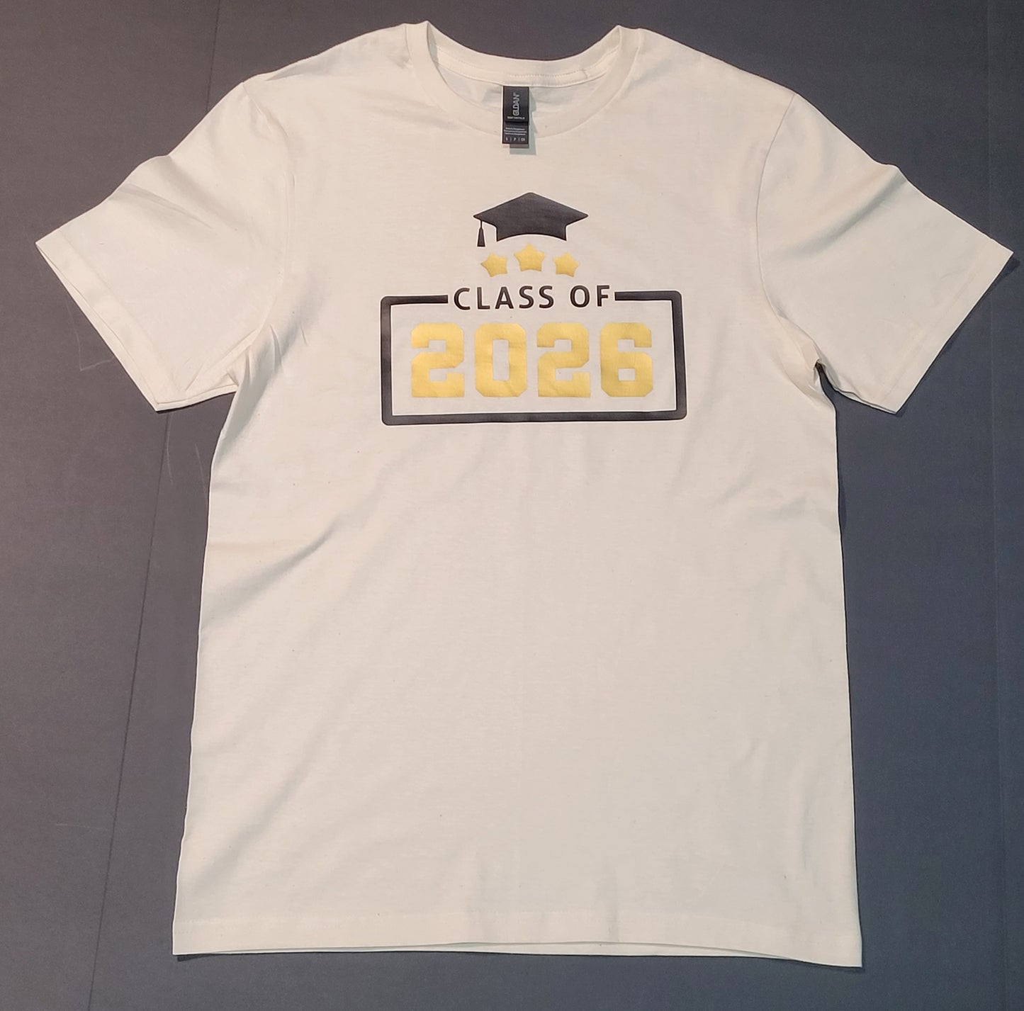 Class of 2026 graduation t-shirt flat lay — white tee with gold and black Class of 2026 design, graduation cap and stars